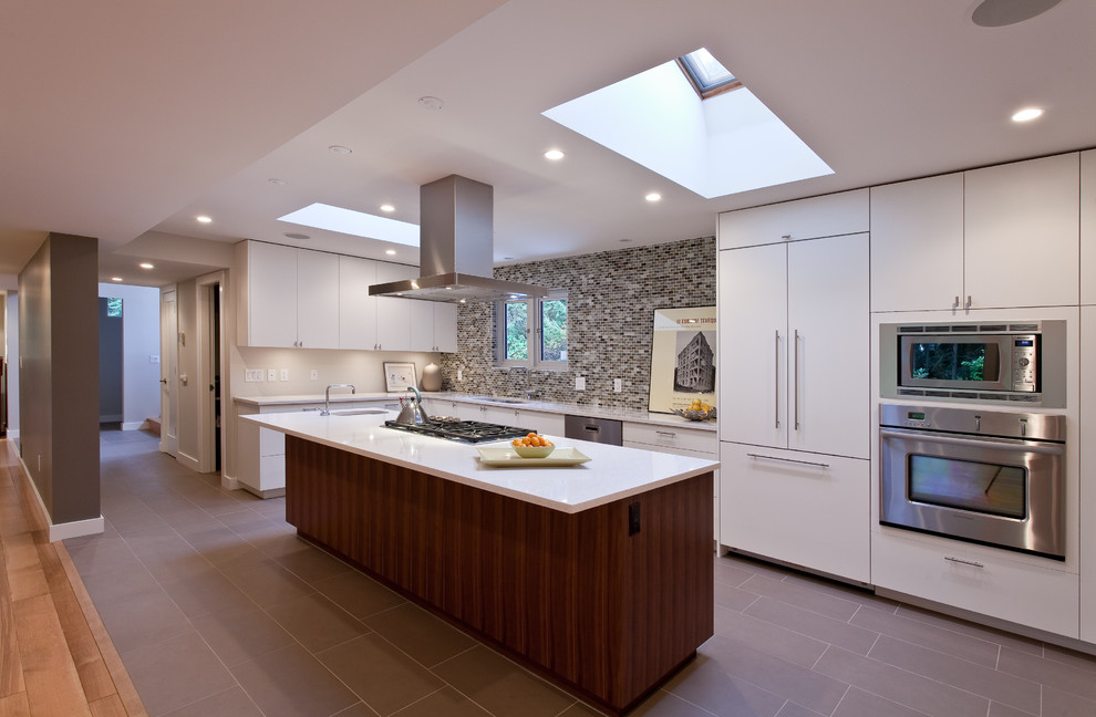 Large contemporary l-shaped open plan kitchen in Vancouver with stainless steel appliances, flat-panel cabinets, white cabinets, multi-coloured splashback, mosaic tile splashback, an undermount sink, quartz benchtops, porcelain floors, with island and brown floor.