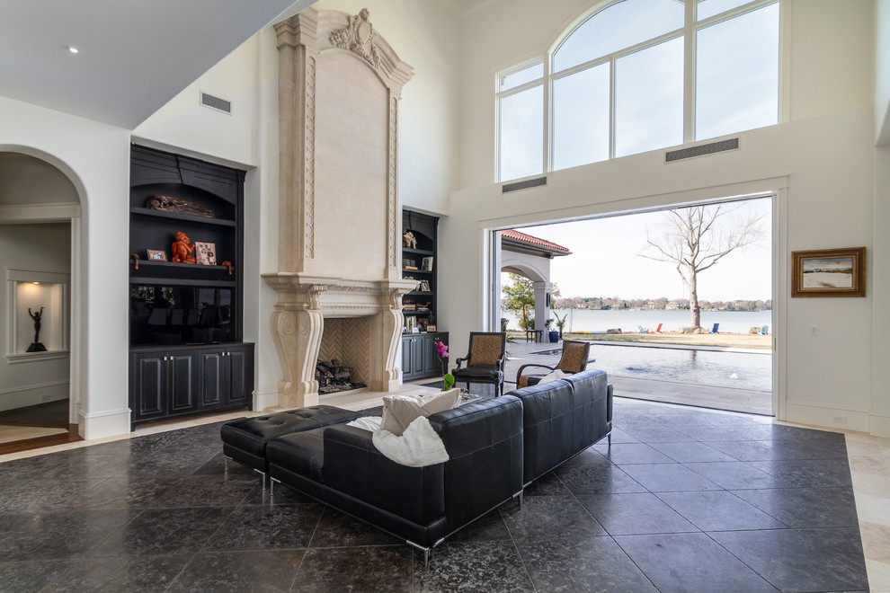 Inspiration for an expansive mediterranean open concept family room in Charlotte with white walls, a standard fireplace, a stone fireplace surround, a freestanding tv, black floor and travertine floors.