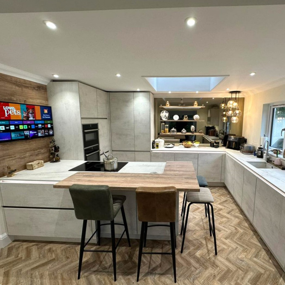 Medium sized modern grey and white u-shaped kitchen/diner in Cardiff with a submerged sink, flat-panel cabinets, distressed cabinets, quartz worktops, black appliances, medium hardwood flooring, an island, brown floors, white worktops and feature lighting.