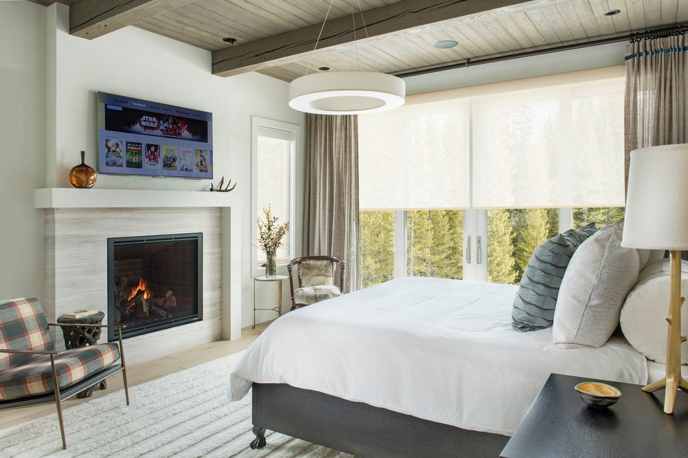 Inspiration for a mid-sized country master bedroom in Other with beige walls, light hardwood floors, a standard fireplace, a tile fireplace surround and brown floor.