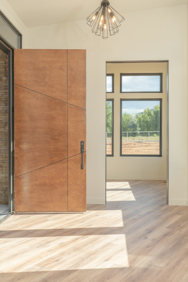 Foto de distribuidor actual extra grande con paredes beige, suelo de madera clara, puerta pivotante, puerta de madera en tonos medios y vigas vistas