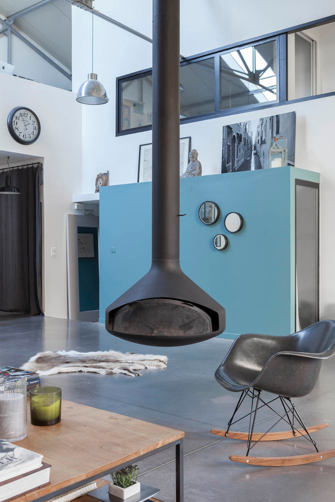 Design ideas for a large industrial open concept family room in Paris with white walls, concrete floors, a hanging fireplace, a metal fireplace surround and grey floor.