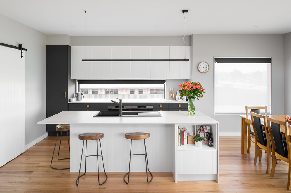 Inspiration for a scandinavian galley open plan kitchen in Hobart with a drop-in sink, flat-panel cabinets, white cabinets, medium hardwood floors, with island, brown floor and white benchtop.