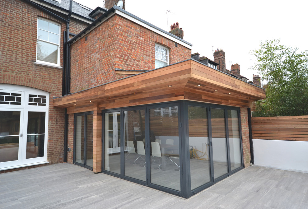 Mid-sized contemporary backyard patio in London with tile and a roof extension.