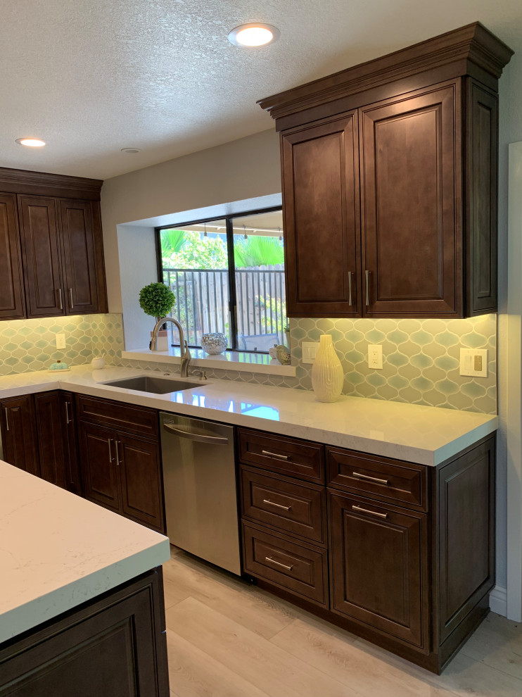 Photo of a mid-sized contemporary l-shaped eat-in kitchen in Sacramento with an undermount sink, raised-panel cabinets, brown cabinets, quartz benchtops, grey splashback, ceramic splashback, stainless steel appliances, vinyl floors, with island, grey floor and white benchtop.