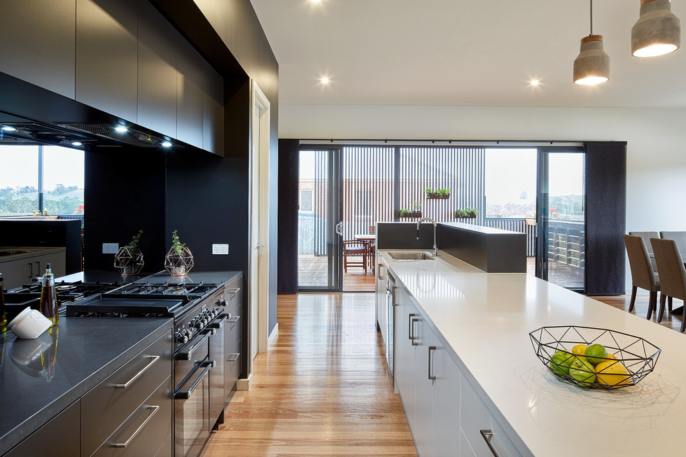 Contemporary galley kitchen in Melbourne with an undermount sink, flat-panel cabinets, black cabinets, black splashback, black appliances, light hardwood floors, with island and beige floor.