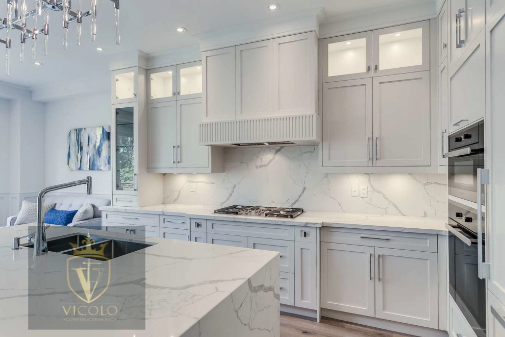 Inspiration for a large transitional l-shaped light wood floor and brown floor kitchen remodel with a double-bowl sink, shaker cabinets, white cabinets, quartz countertops, white backsplash, quartz backsplash, paneled appliances, an island and gray countertops