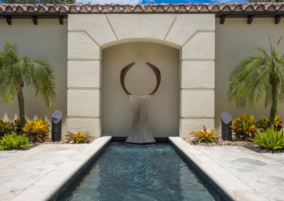 This is an example of a mid-sized modern side yard full sun formal garden in Miami with a water feature and natural stone pavers.