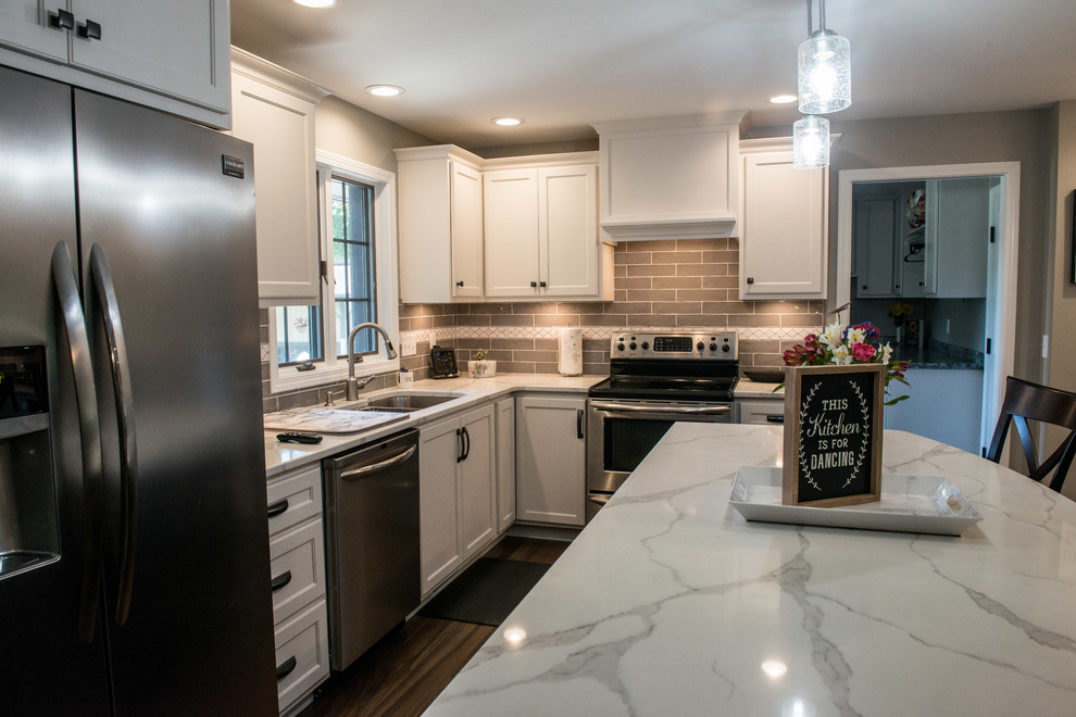 Large transitional u-shaped vinyl floor and brown floor eat-in kitchen photo with a double-bowl sink, shaker cabinets, white cabinets, quartz countertops, gray backsplash, subway tile backsplash, stainless steel appliances, an island and white countertops