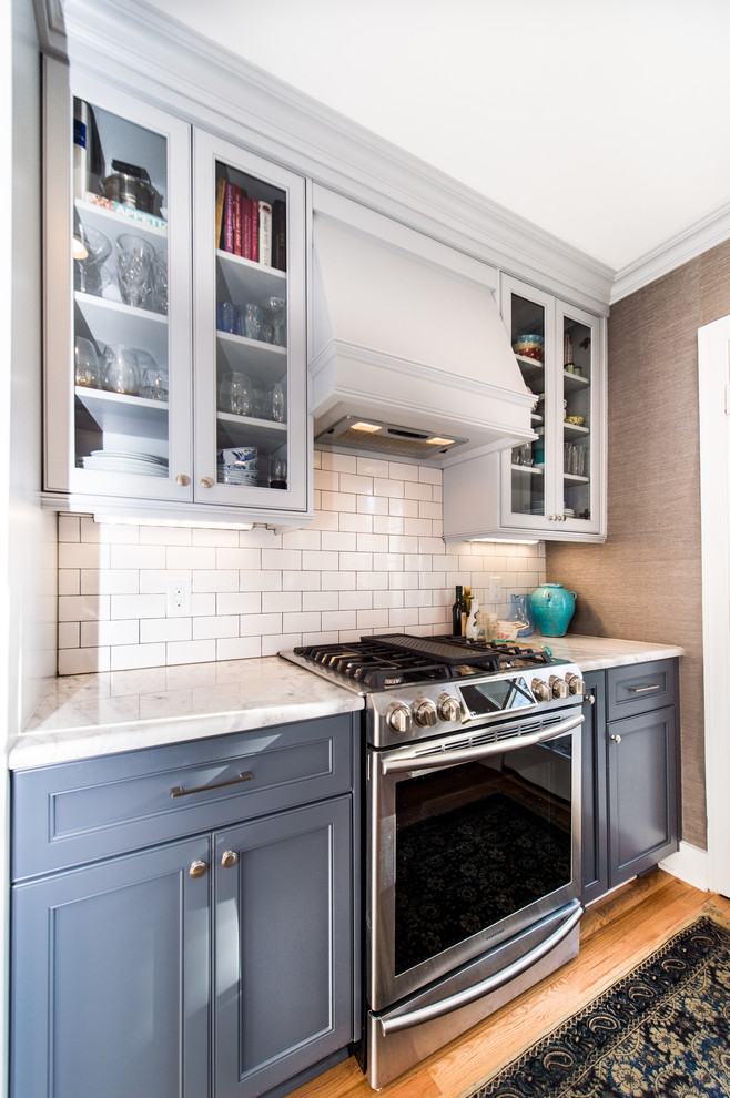 Photo of a contemporary single-wall eat-in kitchen in Charleston with a farmhouse sink, white cabinets, white splashback, subway tile splashback, stainless steel appliances, light hardwood floors and a peninsula.