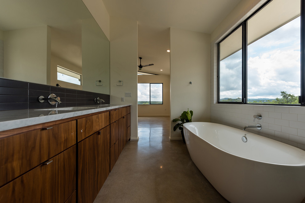 Photo of a large midcentury master bathroom in Austin with flat-panel cabinets, medium wood cabinets, a freestanding tub, a corner shower, a two-piece toilet, black and white tile, subway tile, white walls, concrete floors, an undermount sink and marble benchtops.