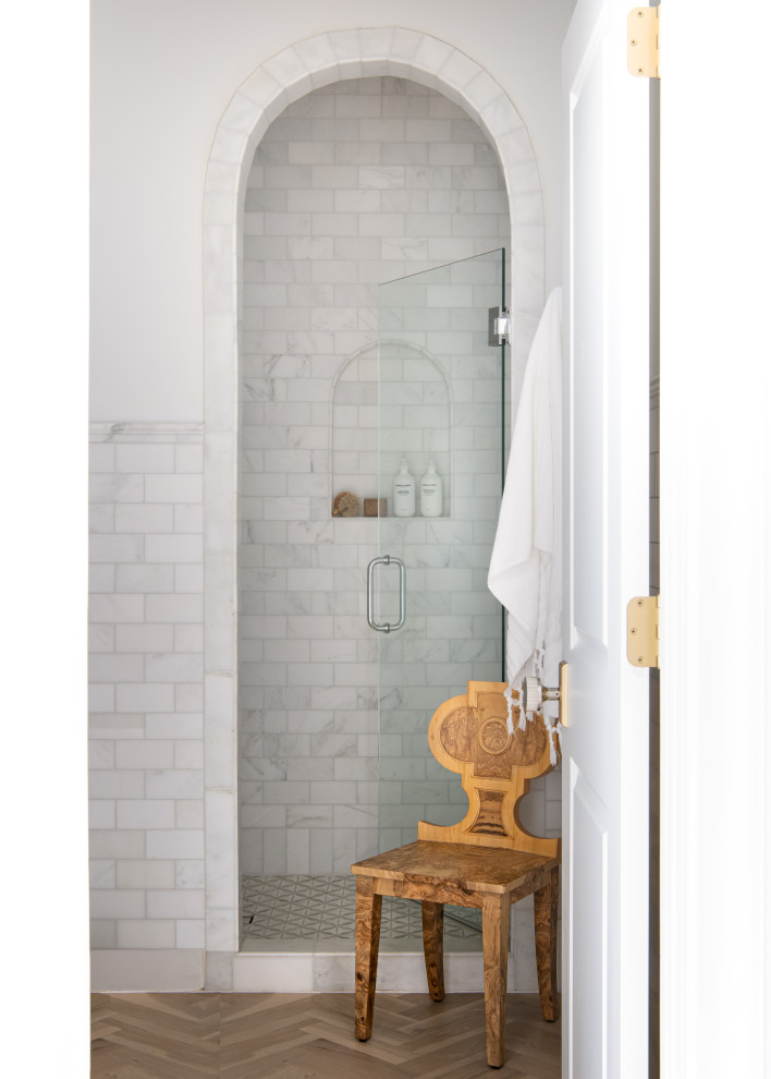Inredning av ett klassiskt stort vit vitt badrum för barn, med möbel-liknande, vita skåp, ett undermonterat badkar, en toalettstol med separat cisternkåpa, vit kakel, marmorkakel, vita väggar, ljust trägolv, ett undermonterad handfat, marmorbänkskiva, brunt golv och dusch med gångjärnsdörr