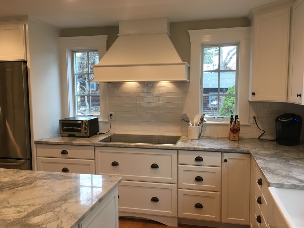 Eat-in kitchen - transitional l-shaped medium tone wood floor eat-in kitchen idea in Boston with a farmhouse sink, shaker cabinets, white cabinets, white backsplash, porcelain backsplash, stainless steel appliances and an island