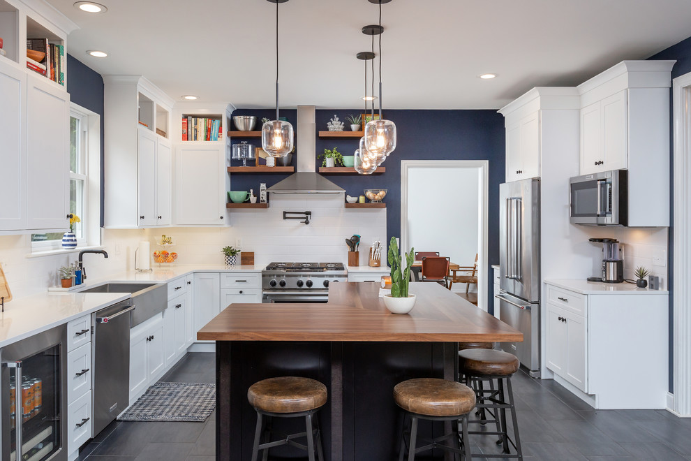 Inspiration for a transitional u-shaped open plan kitchen in Philadelphia with a farmhouse sink, shaker cabinets, white cabinets, white splashback, subway tile splashback, stainless steel appliances, with island, grey floor and white benchtop.