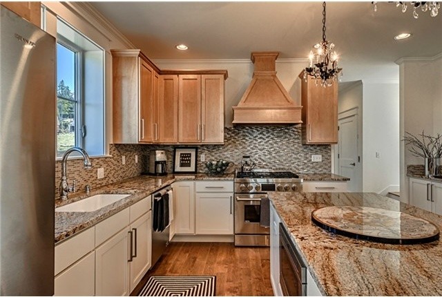 Photo of a beach style l-shaped open plan kitchen in Seattle with shaker cabinets, white cabinets, granite benchtops, brown splashback, glass tile splashback, stainless steel appliances, medium hardwood floors and with island.