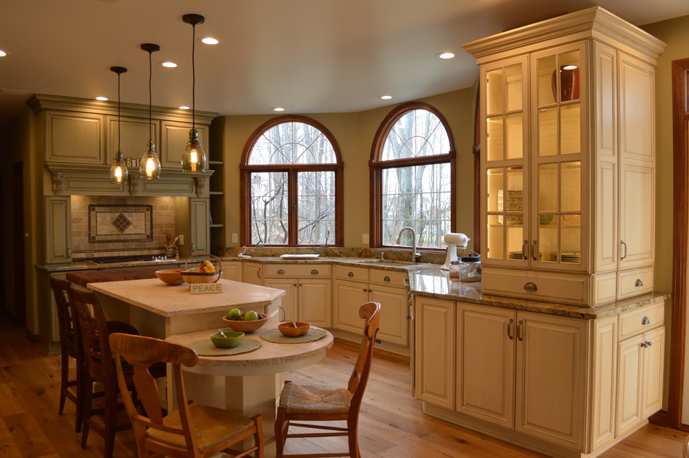 Inspiration for a large timeless u-shaped light wood floor eat-in kitchen remodel in Cleveland with an undermount sink, raised-panel cabinets, green cabinets, limestone countertops, multicolored backsplash, stone tile backsplash, stainless steel appliances and an island