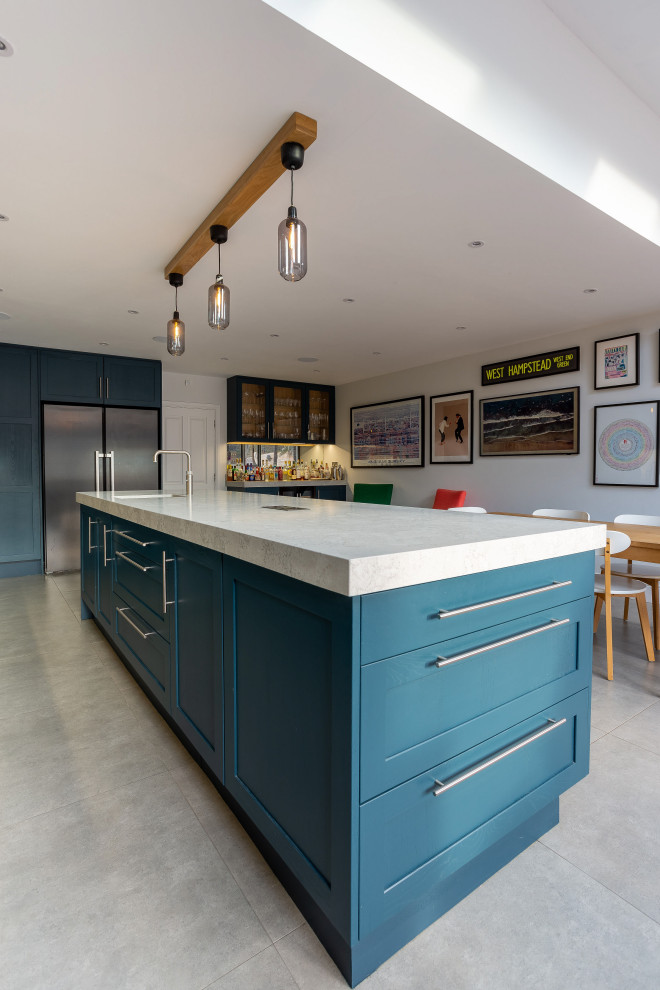 Photo of a large classic kitchen in London with a belfast sink, shaker cabinets, blue cabinets, quartz worktops, grey splashback, mirror splashback, stainless steel appliances, porcelain flooring, an island and grey worktops.