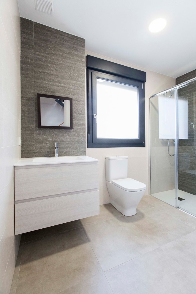 This is an example of a small mediterranean 3/4 bathroom in Other with flat-panel cabinets, light wood cabinets, a curbless shower, a one-piece toilet, beige tile, ceramic tile, beige walls, ceramic floors, an integrated sink, solid surface benchtops, beige floor and a sliding shower screen.