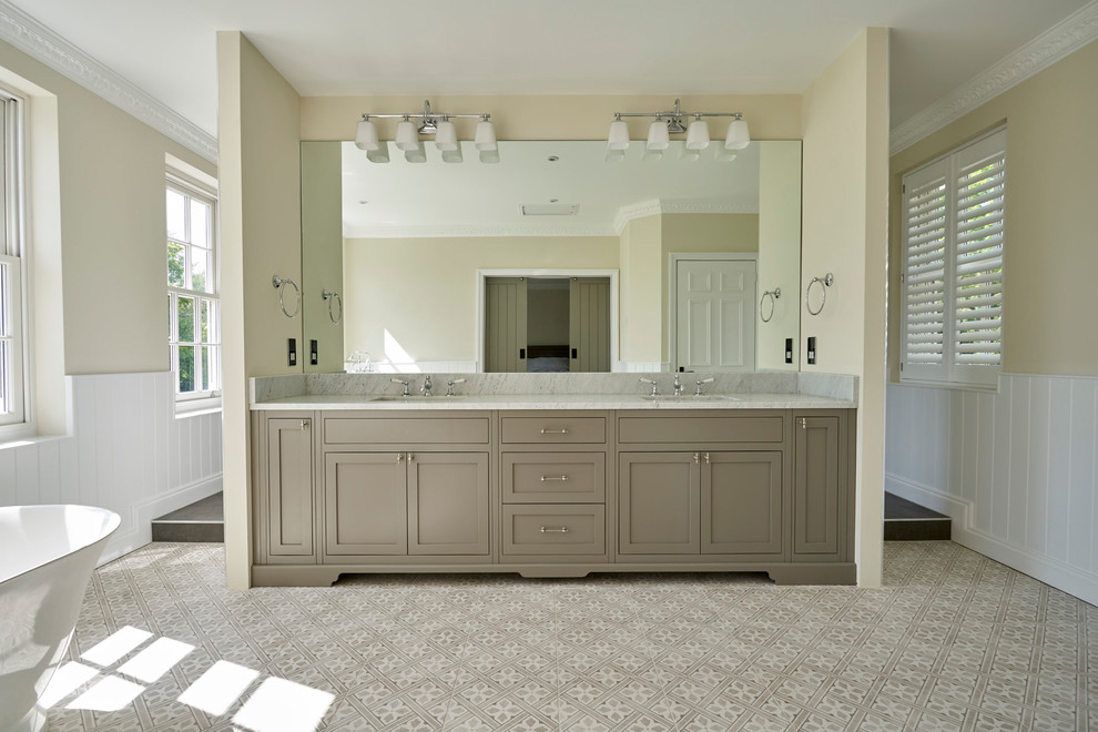 Inspiration for an expansive traditional master bathroom in Sussex with shaker cabinets, beige cabinets, a freestanding tub, an open shower, a one-piece toilet, ceramic floors, marble benchtops, multi-coloured floor, an open shower, beige walls, an undermount sink and grey benchtops.