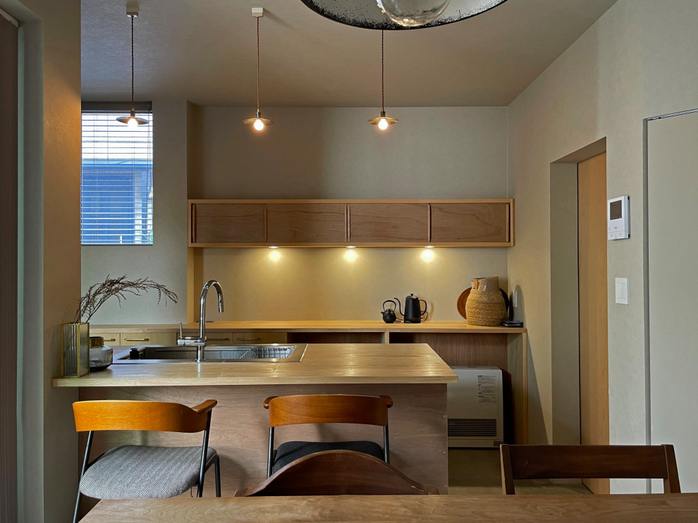 Small scandinavian galley eat-in kitchen in Tokyo with a drop-in sink, flat-panel cabinets, medium wood cabinets, wood benchtops, grey splashback, stainless steel appliances, concrete floors, a peninsula, grey floor, beige benchtop and wallpaper.