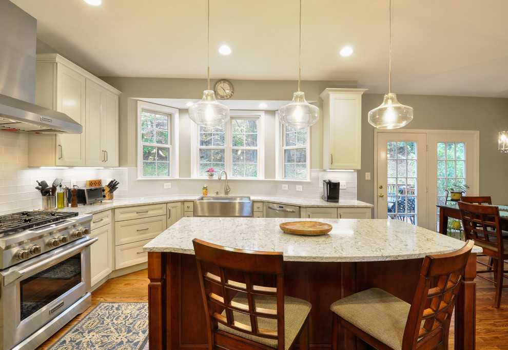 This is an example of a large transitional u-shaped kitchen in DC Metro with a farmhouse sink, recessed-panel cabinets, quartz benchtops, white splashback, stainless steel appliances, medium hardwood floors and with island.