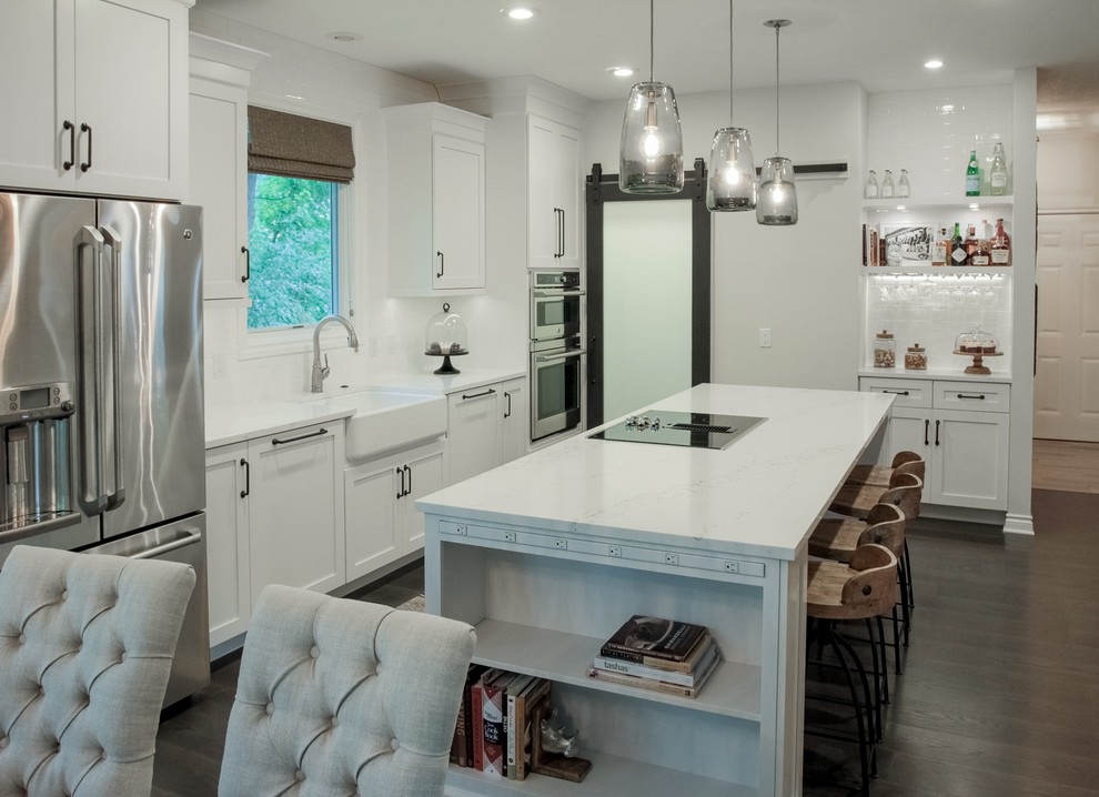 Eat-in kitchen - mid-sized transitional galley dark wood floor eat-in kitchen idea in Grand Rapids with a farmhouse sink, shaker cabinets, white cabinets, quartz countertops, white backsplash, ceramic backsplash, stainless steel appliances and an island