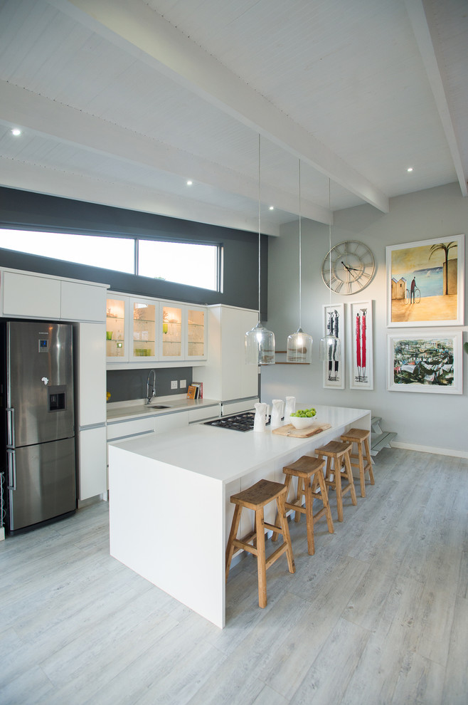 Photo of a contemporary galley open plan kitchen in Other with flat-panel cabinets, white cabinets, grey splashback, stainless steel appliances, light hardwood floors, with island and grey floor.