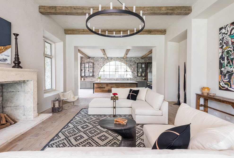Large country open concept living room in Houston with light hardwood floors, a stone fireplace surround, white walls, a standard fireplace and beige floor.