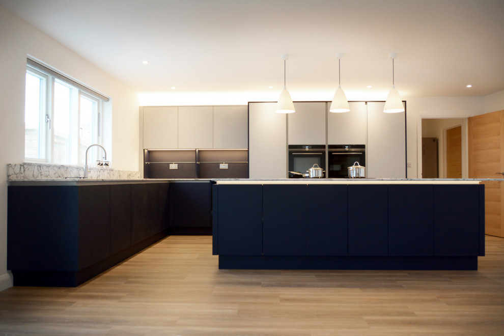 This is an example of a mid-sized contemporary l-shaped open plan kitchen in Cornwall with flat-panel cabinets, blue cabinets, quartzite benchtops and with island.