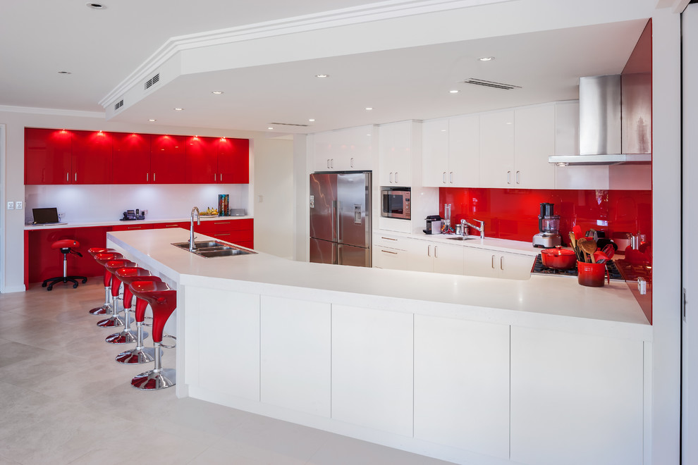 Contemporary kitchen in Perth with a drop-in sink, flat-panel cabinets, red cabinets, solid surface benchtops, red splashback, glass sheet splashback, stainless steel appliances and white benchtop.