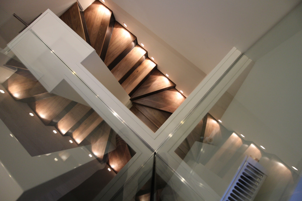 Cette image montre un escalier design en U de taille moyenne avec des marches en bois, des contremarches en bois, un garde-corps en verre, un mur en parement de brique et éclairage.