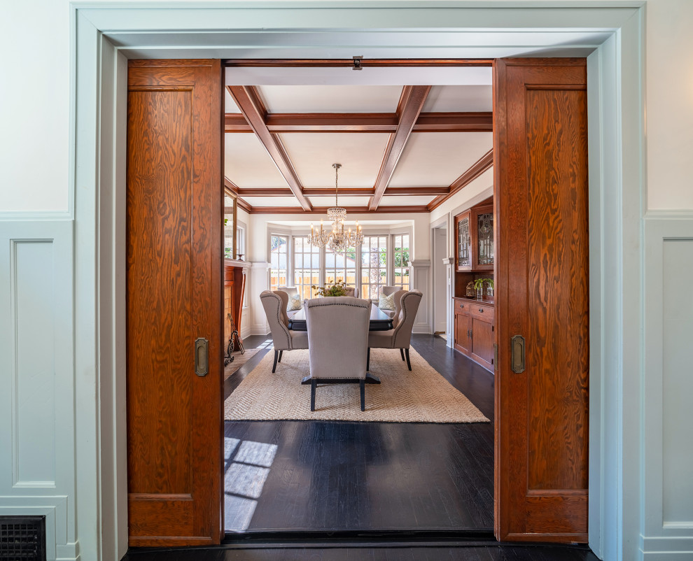 Large arts and crafts separate dining room in Orange County with grey walls, dark hardwood floors, a standard fireplace, a tile fireplace surround, black floor, coffered and decorative wall panelling.