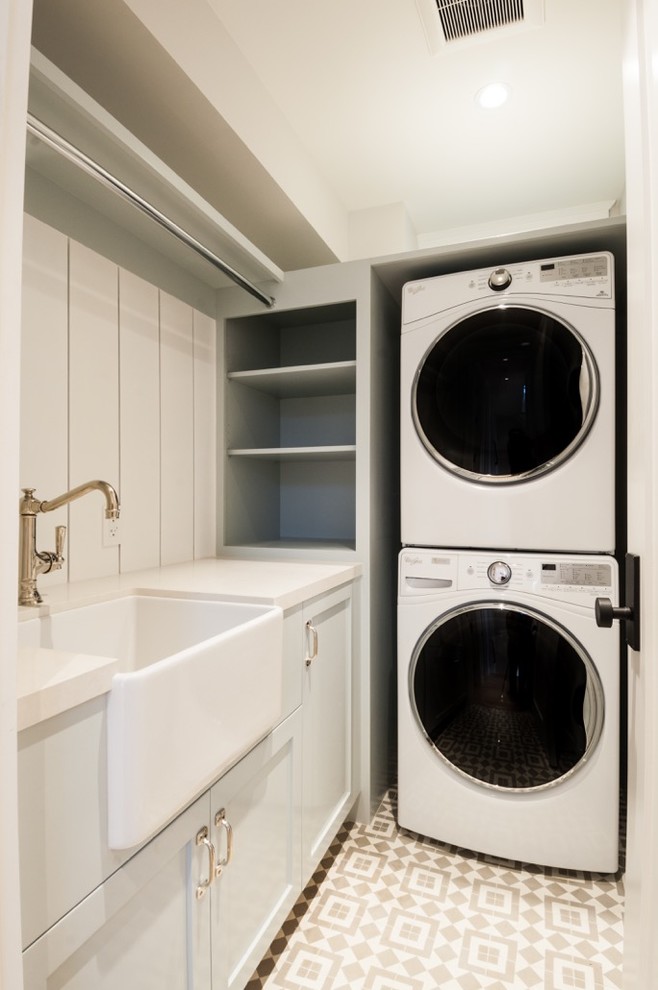 This is an example of a small country l-shaped laundry room in Los Angeles with a farmhouse sink, white cabinets, beige walls and a stacked washer and dryer.