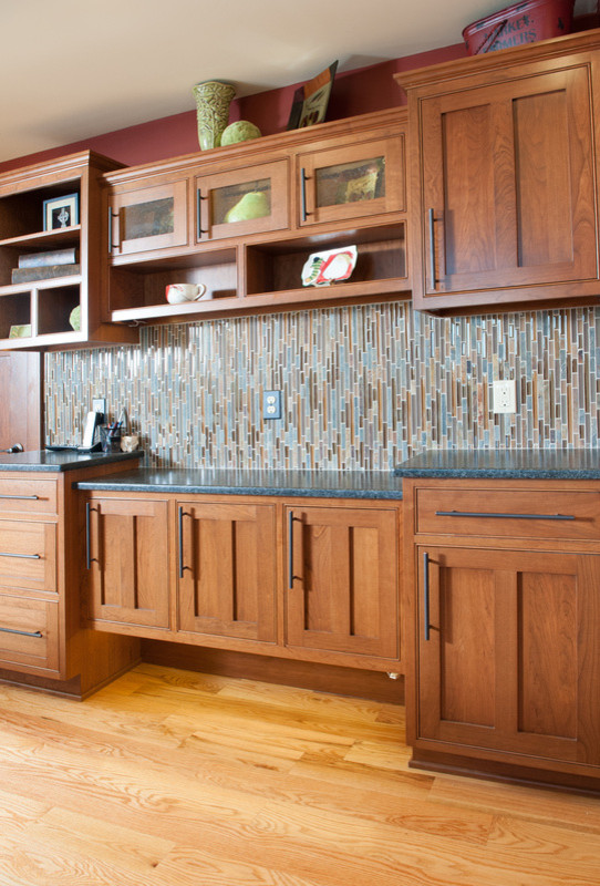 Example of a mid-sized transitional l-shaped medium tone wood floor eat-in kitchen design in Orange County with a farmhouse sink, shaker cabinets, medium tone wood cabinets, granite countertops, multicolored backsplash, matchstick tile backsplash, stainless steel appliances and an island