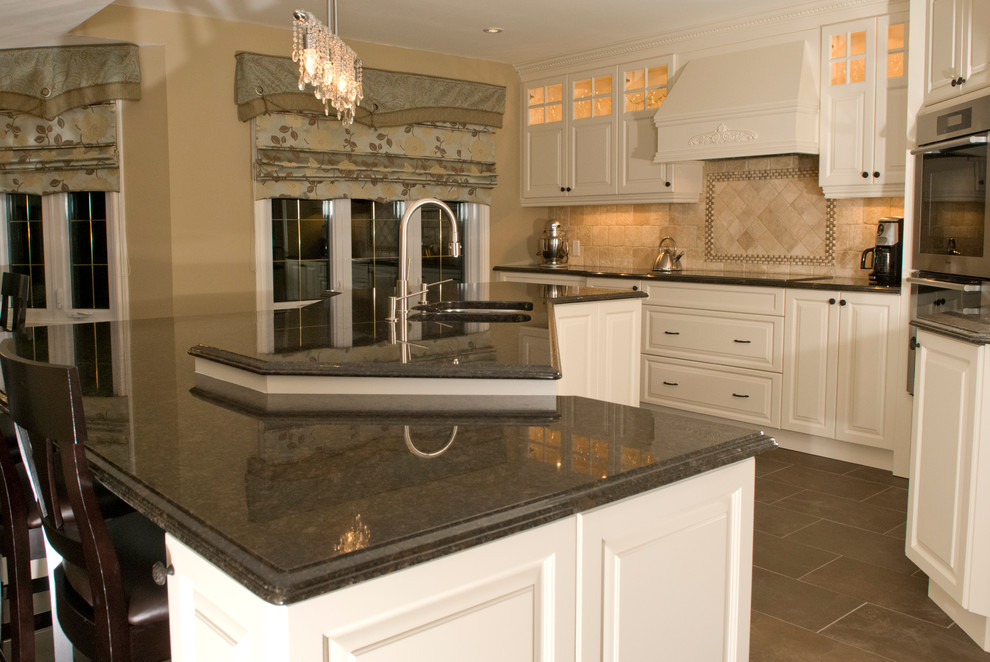 Large traditional l-shaped eat-in kitchen in Montreal with an undermount sink, raised-panel cabinets, white cabinets, granite benchtops, beige splashback, travertine splashback, stainless steel appliances, ceramic floors, with island, brown floor and brown benchtop.