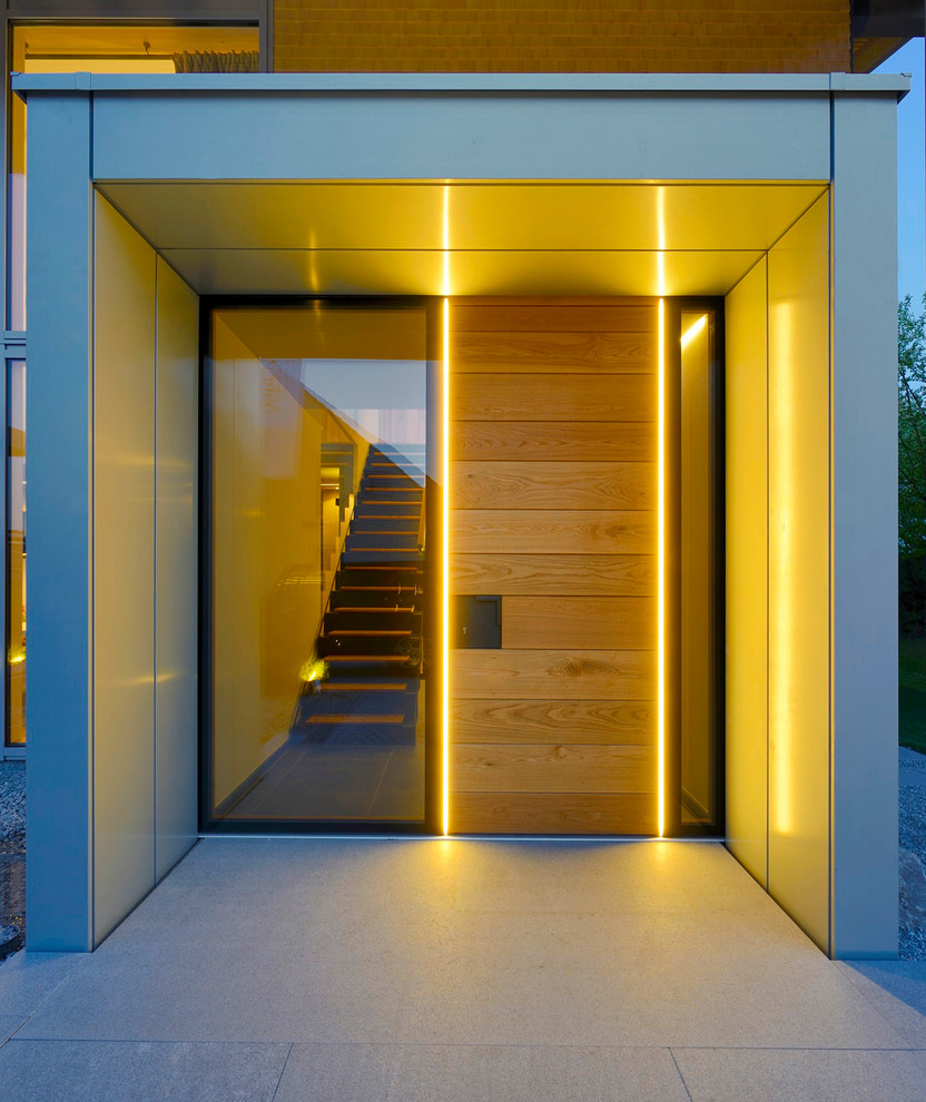 This is an example of a contemporary front door in Other with a single front door, a light wood front door, grey walls and concrete floors.