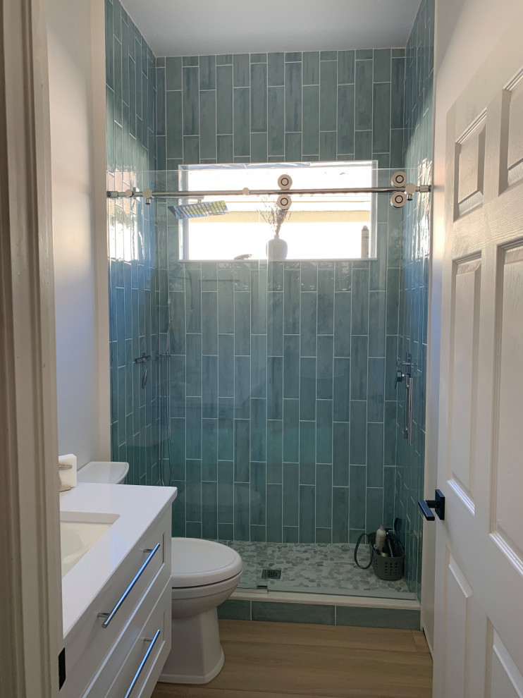 This is an example of a small coastal shower room bathroom in Miami with shaker cabinets, white cabinets, an alcove shower, a two-piece toilet, blue tiles, metro tiles, white walls, porcelain flooring, a submerged sink, engineered stone worktops, multi-coloured floors, a sliding door, white worktops, a single sink and a floating vanity unit.