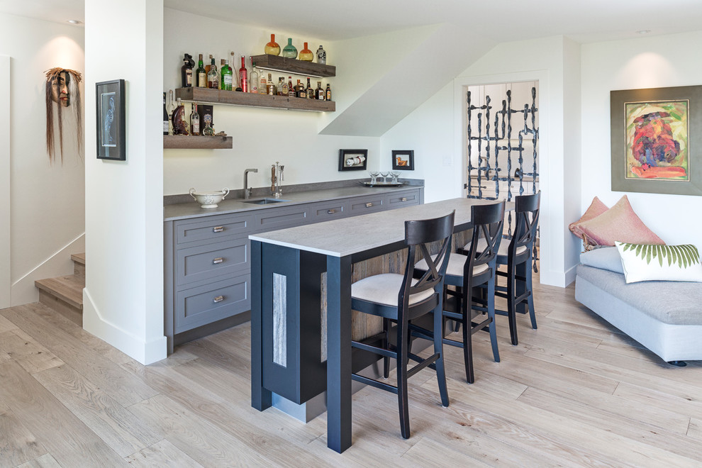 This is an example of a large transitional galley seated home bar in Calgary with an undermount sink, quartzite benchtops, light hardwood floors, open cabinets and beige floor.