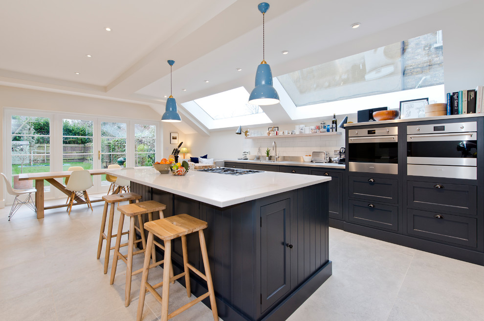 Design ideas for a large contemporary single-wall eat-in kitchen in London with an undermount sink, shaker cabinets, black cabinets, quartzite benchtops, white splashback, subway tile splashback, stainless steel appliances, with island, grey floor and white benchtop.