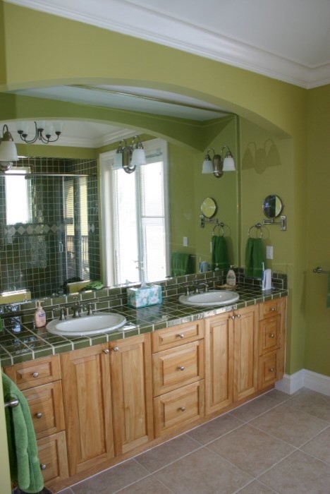 This is an example of a large tropical master bathroom in Other with a drop-in sink, raised-panel cabinets, light wood cabinets, tile benchtops, an open shower, a one-piece toilet, green tile, ceramic tile, green walls and ceramic floors.