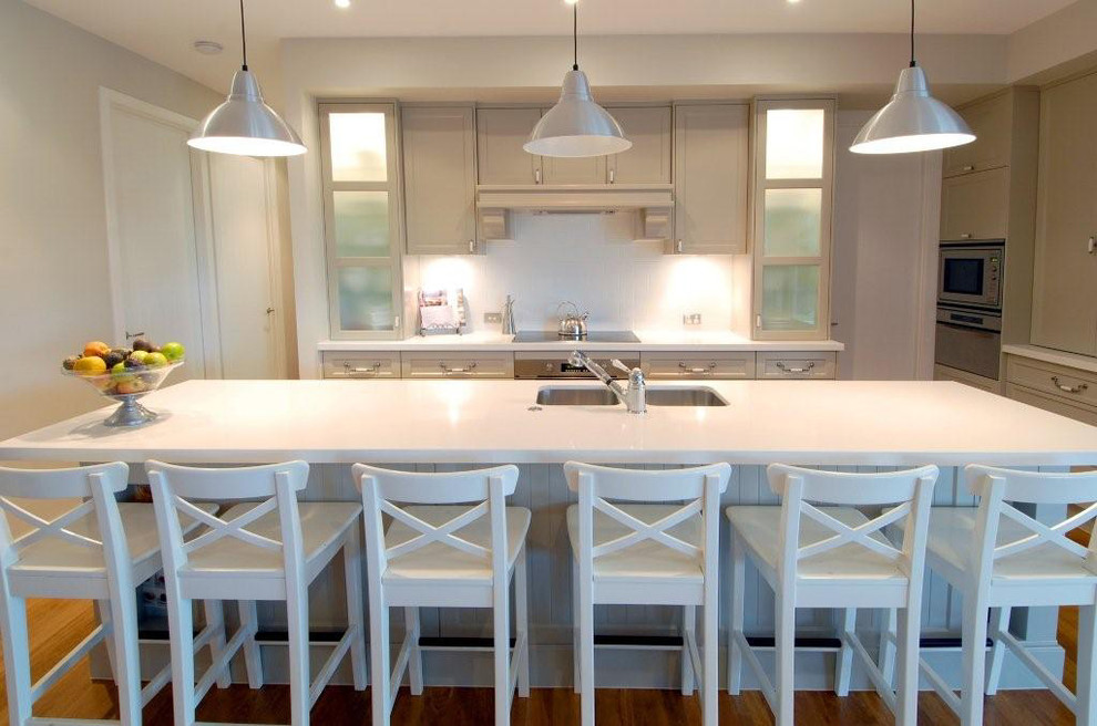 Large traditional eat-in kitchen in Brisbane with recessed-panel cabinets, white splashback, light hardwood floors and with island.