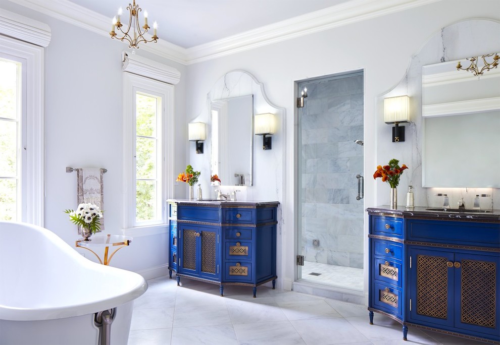 This is an example of a contemporary bathroom in San Francisco with blue cabinets, a freestanding tub, white tile, white walls, porcelain floors, an undermount sink, quartzite benchtops, grey floor and black benchtops.