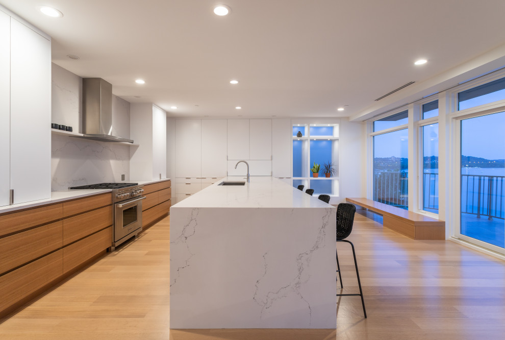 Design ideas for a large modern galley eat-in kitchen in Cincinnati with an undermount sink, flat-panel cabinets, light wood cabinets, quartz benchtops, white splashback, stone slab splashback, stainless steel appliances, light hardwood floors, with island and white benchtop.