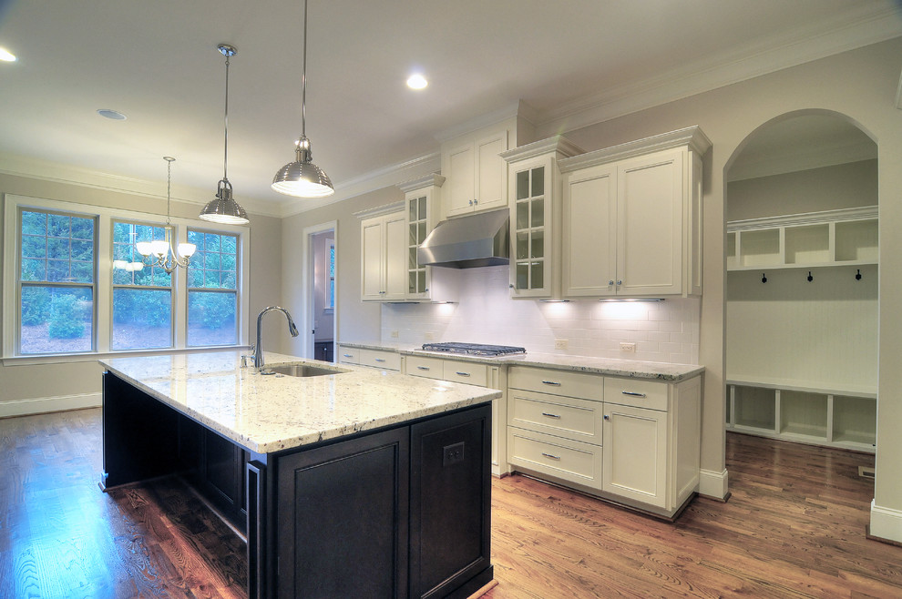 Example of a large transitional l-shaped medium tone wood floor open concept kitchen design in Charlotte with an island, an undermount sink, recessed-panel cabinets, white cabinets, granite countertops, white backsplash, subway tile backsplash and stainless steel appliances