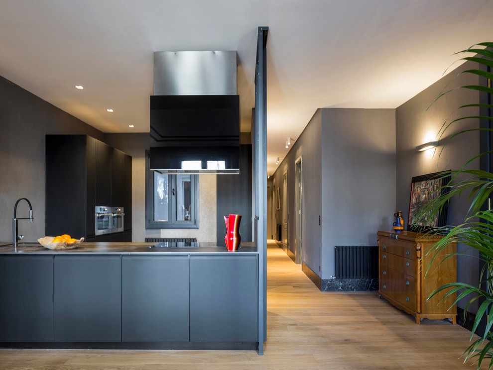 Inspiration for a mid-sized contemporary open plan kitchen in Bilbao with flat-panel cabinets, black cabinets, stainless steel appliances, a peninsula and light hardwood floors.