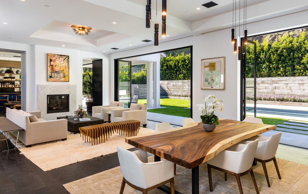 Transitional open plan dining in Los Angeles with white walls, dark hardwood floors, a standard fireplace, a stone fireplace surround and brown floor.