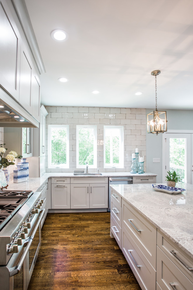 Photo of a transitional u-shaped eat-in kitchen in Charlotte with shaker cabinets, grey cabinets, white splashback, subway tile splashback, stainless steel appliances, medium hardwood floors, with island, brown floor and white benchtop.