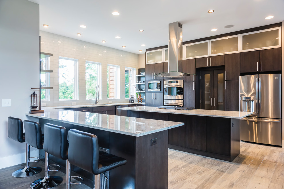 Design ideas for a large modern u-shaped open plan kitchen in Raleigh with an undermount sink, flat-panel cabinets, dark wood cabinets, granite benchtops, grey splashback, glass tile splashback, stainless steel appliances, light hardwood floors, a peninsula, brown floor and grey benchtop.