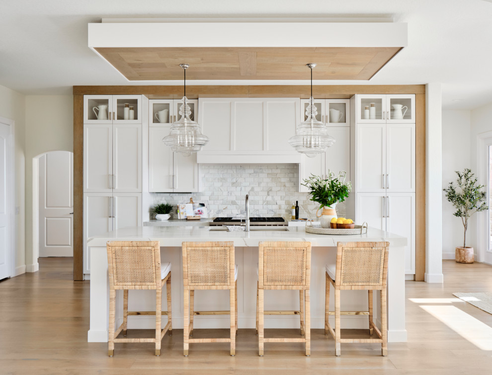 Large traditional l-shaped open plan kitchen in Austin with a submerged sink, shaker cabinets, white cabinets, engineered stone countertops, white splashback, marble splashback, stainless steel appliances, light hardwood flooring, an island, grey floors, white worktops and a wood ceiling.