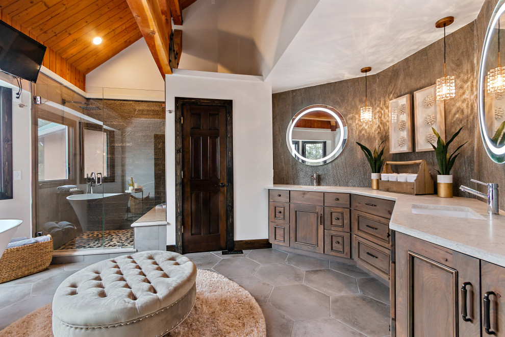 Photo of a large master bathroom in Denver with recessed-panel cabinets, medium wood cabinets, a freestanding tub, an alcove shower, a two-piece toilet, gray tile, porcelain tile, grey walls, porcelain floors, an undermount sink, quartzite benchtops, grey floor, a hinged shower door, white benchtops, a shower seat, a double vanity, a built-in vanity and exposed beam.